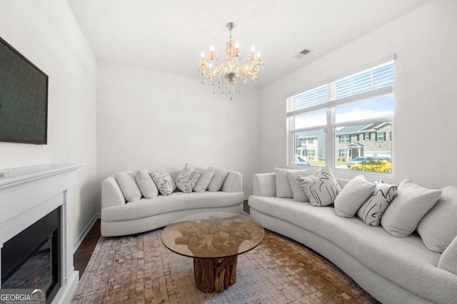 living area with wood finished floors, a glass covered fireplace, baseboards, a notable chandelier, and visible vents