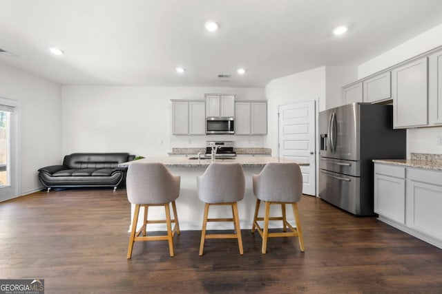 kitchen with light stone countertops, stainless steel appliances, a kitchen breakfast bar, and recessed lighting