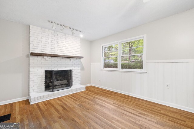 unfurnished living room with a fireplace, track lighting, wood finished floors, and wainscoting