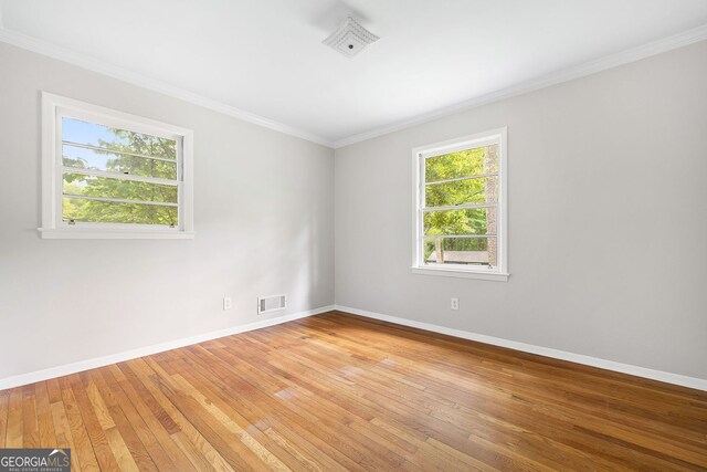 empty room featuring baseboards, visible vents, light wood-style floors, and crown molding