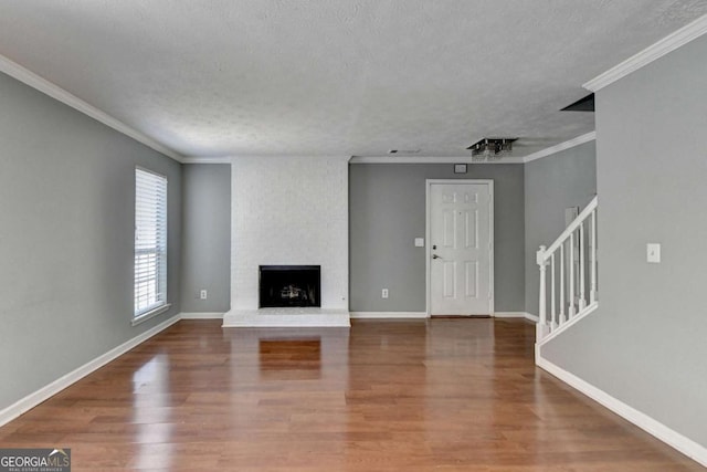 unfurnished living room featuring crown molding, stairs, wood finished floors, a textured ceiling, and a fireplace