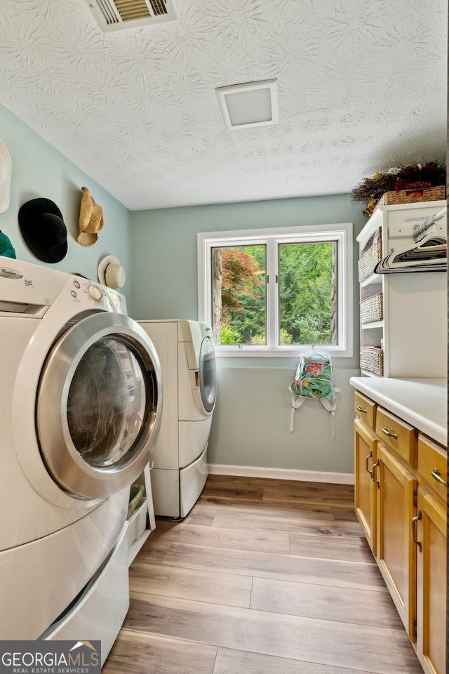4761 Gateway Ln, Flowery Branch, GA 30542 - laundry room with light wood-type flooring, cabinet space, washing machine and dryer, and a textured ceiling