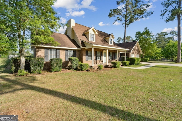 view of front of property featuring a chimney, brick siding, a porch, and a front yard