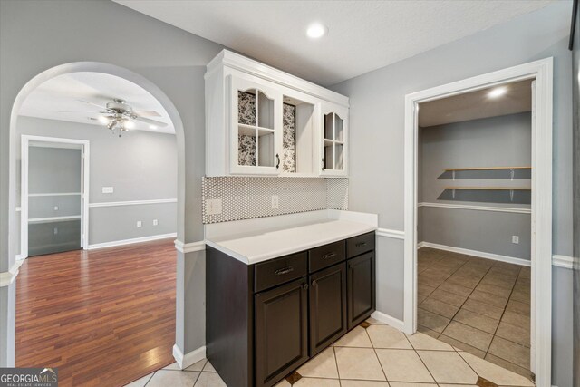 kitchen featuring white cabinets, arched walkways, glass insert cabinets, a ceiling fan, and light countertops