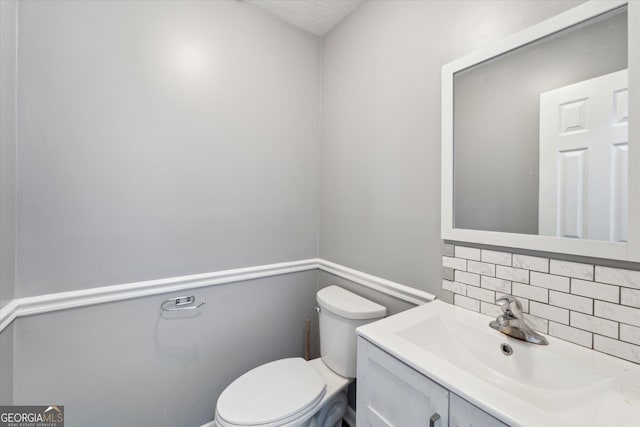half bathroom featuring tasteful backsplash, a textured ceiling, toilet, and vanity