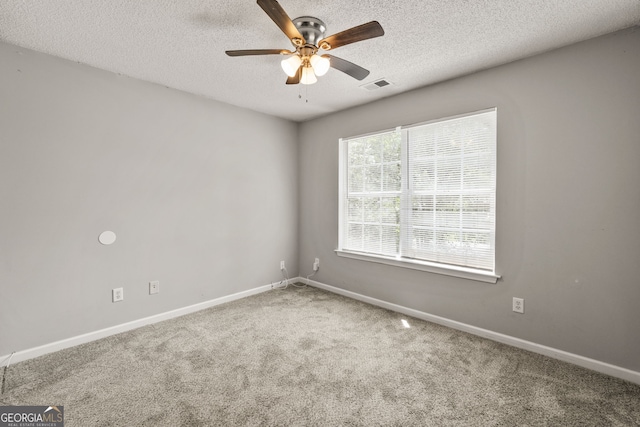 carpeted spare room with baseboards, a ceiling fan, a textured ceiling, and visible vents