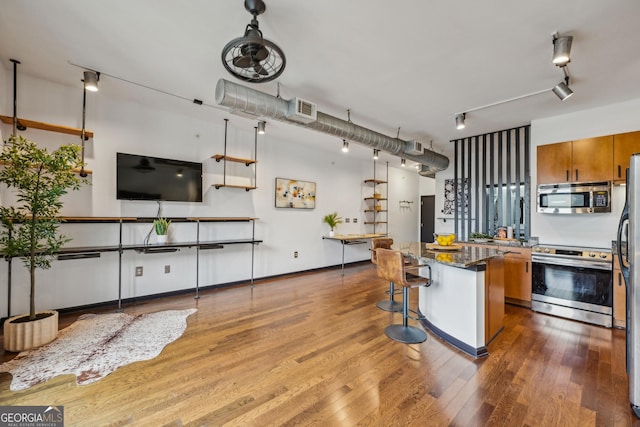 5300 Peachtree Rd Unit 3601, Atlanta, GA 30341 - kitchen with appliances with stainless steel finishes, brown cabinetry, wood finished floors, a center island, and a kitchen breakfast bar
