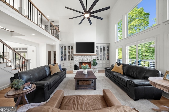 living area featuring stairway, a towering ceiling, wood finished floors, a fireplace, and ceiling fan