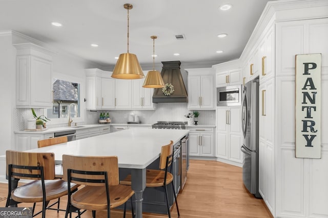 kitchen with white cabinets, stainless steel appliances, a breakfast bar area, and premium range hood