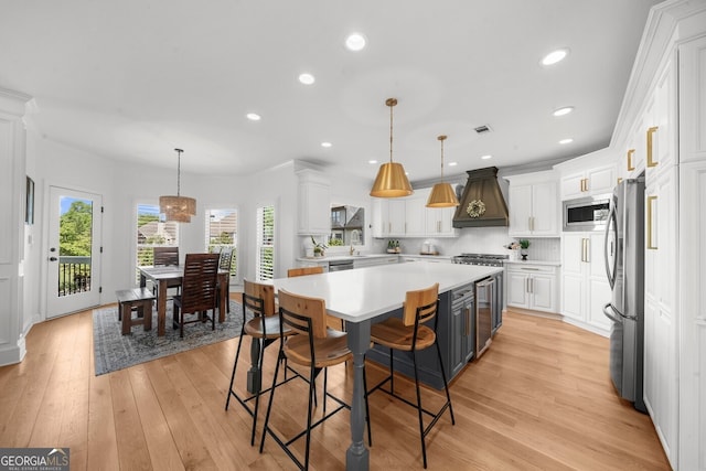 kitchen featuring white cabinets, stainless steel appliances, light countertops, a center island, and custom range hood
