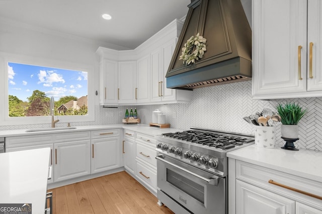 kitchen featuring a sink, white cabinetry, custom range hood, backsplash, and high end stainless steel range oven