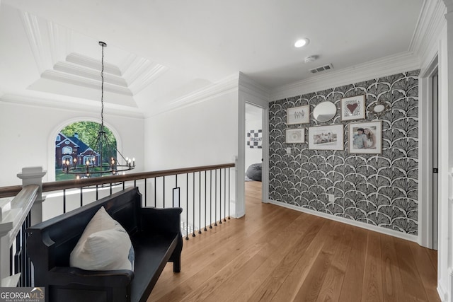 corridor featuring a raised ceiling, wood finished floors, visible vents, crown molding, and a notable chandelier