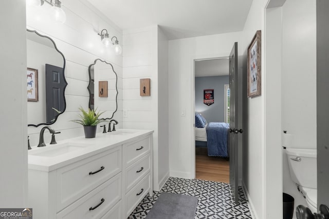 ensuite bathroom with double vanity, tile patterned floors, baseboards, and a sink