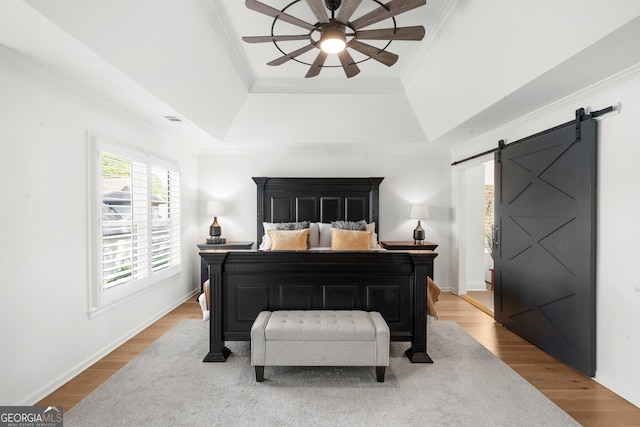 bedroom with a barn door, a raised ceiling, wood finished floors, ornamental molding, and ceiling fan