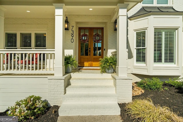 view of exterior entry with covered porch, brick siding, and french doors