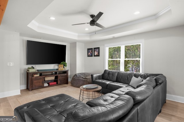 living room featuring a raised ceiling, light wood-style flooring, a ceiling fan, and ornamental molding