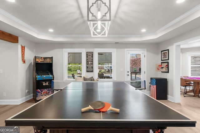 rec room with a tray ceiling, baseboards, recessed lighting, light wood-style floors, and crown molding
