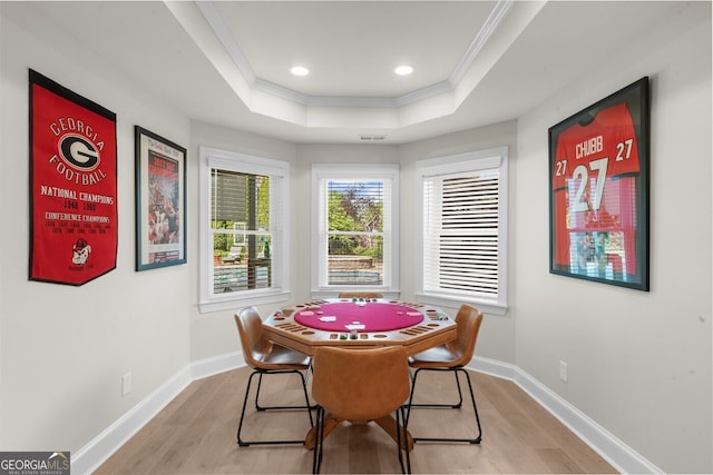 dining room featuring light wood finished floors, baseboards, a tray ceiling, and crown molding
