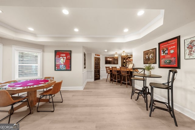 dining space featuring ornamental molding, a tray ceiling, and light wood-type flooring