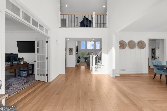 foyer entrance featuring french doors, a towering ceiling, stairs, crown molding, and hardwood / wood-style floors