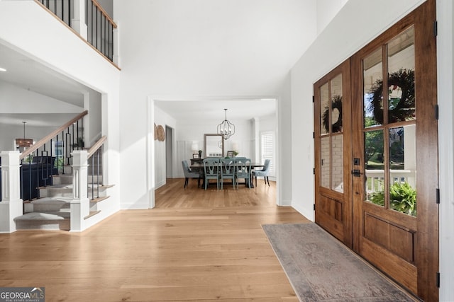 foyer entrance featuring stairway, a towering ceiling, an inviting chandelier, light wood-style floors, and baseboards
