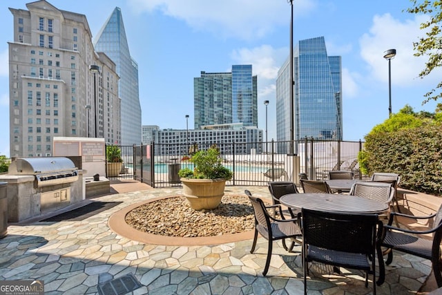 view of patio / terrace with fence, an outdoor kitchen, area for grilling, a community pool, and a view of city