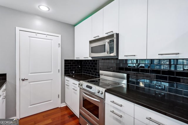 kitchen with dark countertops, dark wood-type flooring, tasteful backsplash, appliances with stainless steel finishes, and white cabinetry