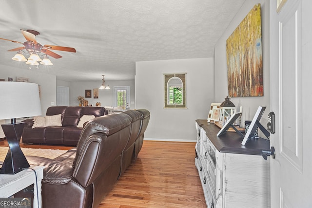living area featuring baseboards, a ceiling fan, a textured ceiling, and light wood-type flooring