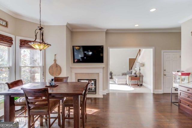 dining space featuring dark wood-style flooring, ornamental molding, a tile fireplace, and baseboards