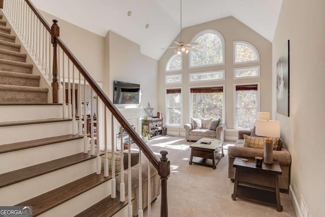 carpeted living room featuring high vaulted ceiling, stairs, and ceiling fan