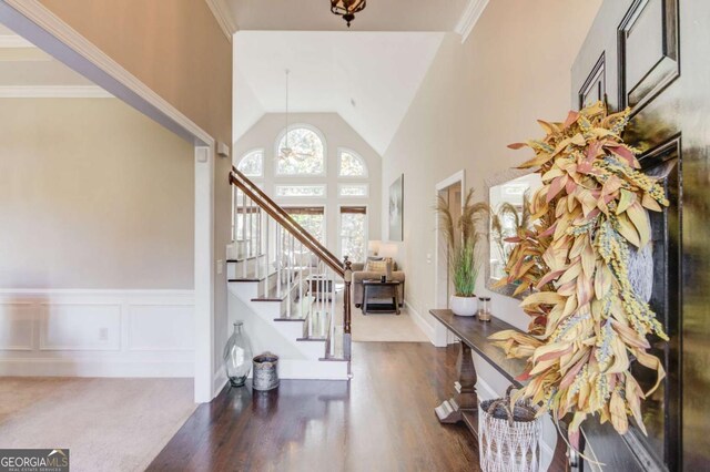 foyer featuring a wainscoted wall, an inviting chandelier, wood finished floors, stairs, and high vaulted ceiling