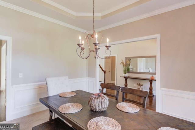 dining space with wainscoting, a chandelier, crown molding, a decorative wall, and a raised ceiling