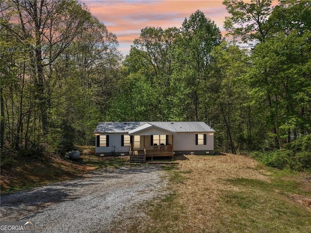manufactured / mobile home featuring gravel driveway, a view of trees, and a deck