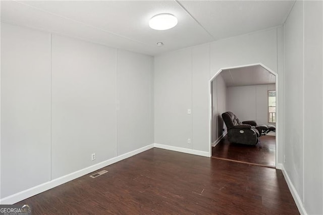 unfurnished room with arched walkways, wood finished floors, visible vents, and baseboards