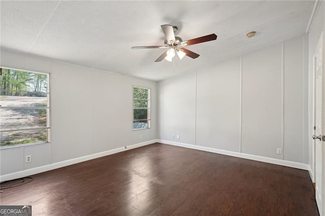 unfurnished room with a wealth of natural light, a ceiling fan, dark wood-style flooring, and baseboards