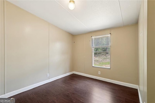 spare room featuring baseboards and dark wood finished floors