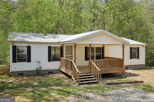 view of front of house with crawl space, a view of trees, a porch, and metal roof