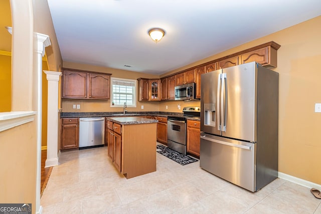 kitchen featuring glass insert cabinets, a sink, dark countertops, stainless steel appliances, and a center island
