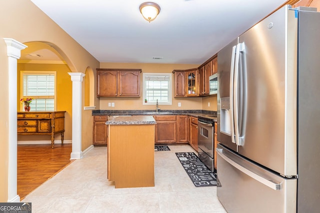 kitchen with arched walkways, appliances with stainless steel finishes, a kitchen island, a sink, and ornate columns