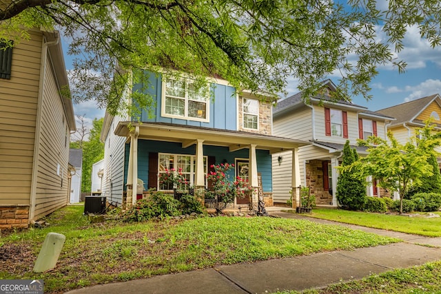 traditional-style home with a porch, a front yard, central AC unit, stone siding, and board and batten siding