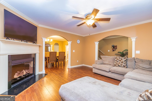living area with arched walkways, wood finished floors, decorative columns, ceiling fan, and a fireplace with raised hearth