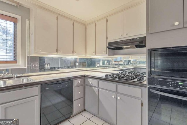 kitchen with black appliances, under cabinet range hood, light tile patterned floors, and a sink