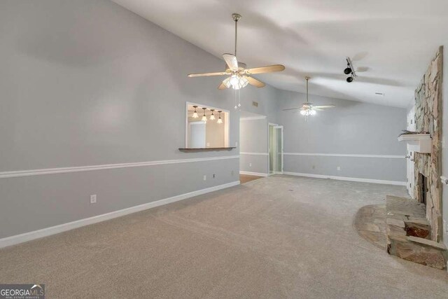 unfurnished living room with light carpet, lofted ceiling, a ceiling fan, a stone fireplace, and baseboards