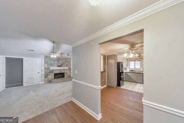 unfurnished living room with ceiling fan, light wood-type flooring, crown molding, a fireplace, and baseboards