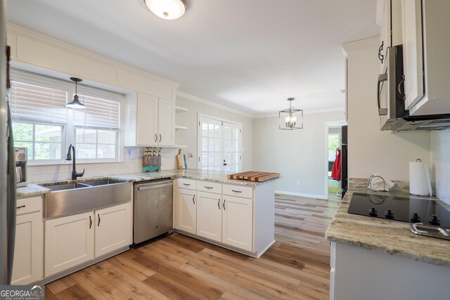 kitchen featuring light wood finished floors, a peninsula, a wealth of natural light, appliances with stainless steel finishes, and ornamental molding