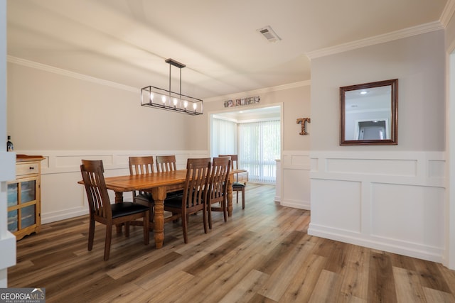 dining area with a decorative wall, wood finished floors, visible vents, and crown molding