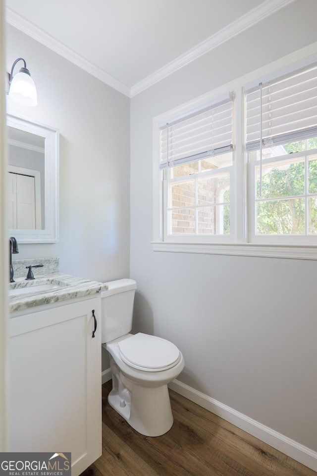 half bath with crown molding, wood finished floors, vanity, baseboards, and toilet