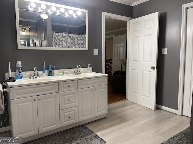 bathroom with crown molding, wood finished floors, a sink, and double vanity