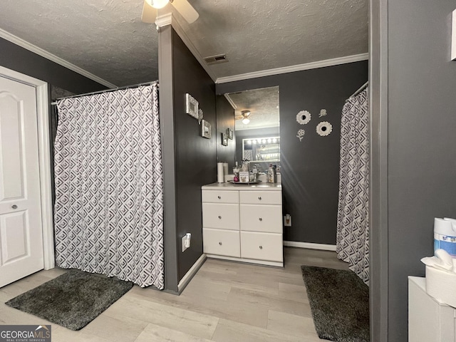 bathroom with a textured ceiling, a ceiling fan, wood finished floors, vanity, and ornamental molding