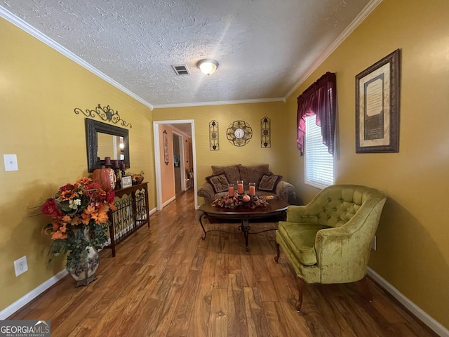 living room with wood finished floors, a textured ceiling, baseboards, ornamental molding, and visible vents